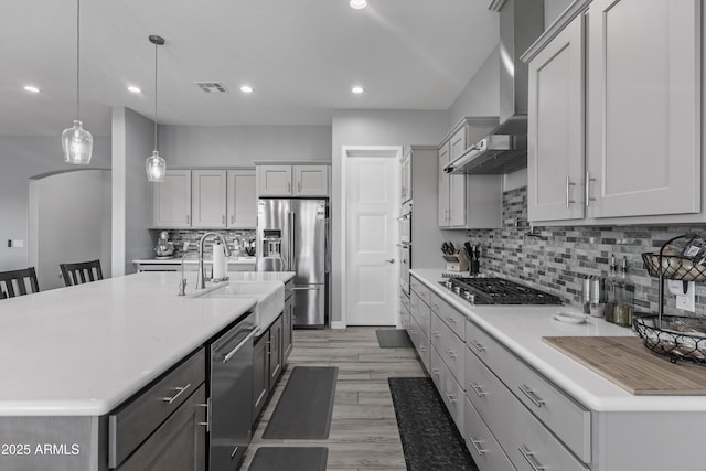 kitchen with arched walkways, a sink, stainless steel appliances, light countertops, and wall chimney range hood