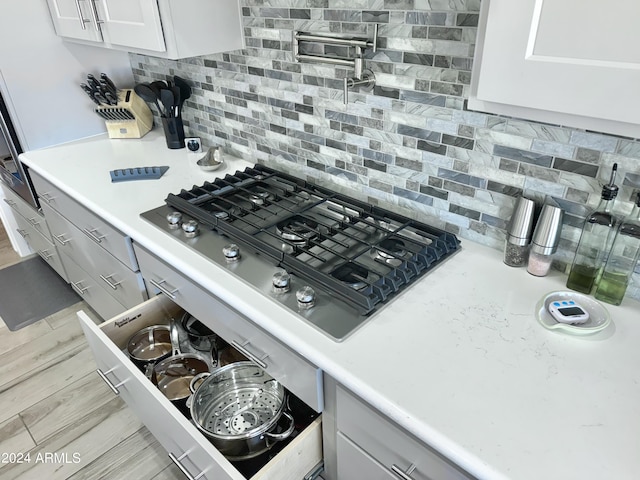 kitchen featuring light wood finished floors, backsplash, stainless steel gas cooktop, light countertops, and white cabinetry