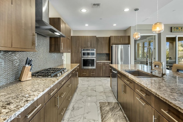 kitchen featuring light stone countertops, stainless steel appliances, sink, wall chimney range hood, and decorative light fixtures