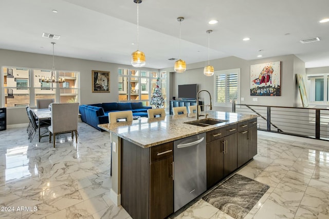 kitchen featuring pendant lighting, sink, light stone countertops, an island with sink, and dark brown cabinetry