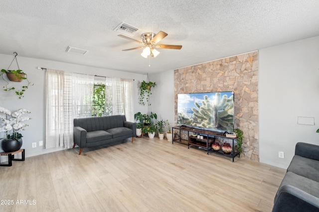 living area featuring light wood-type flooring, a ceiling fan, visible vents, and a textured ceiling