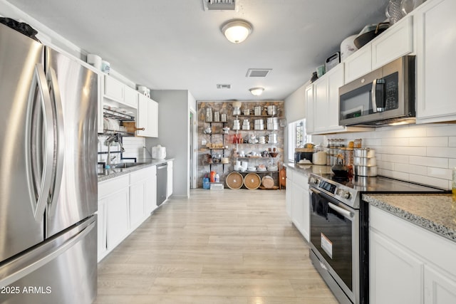 kitchen with light wood-style flooring, stainless steel appliances, a sink, white cabinetry, and tasteful backsplash