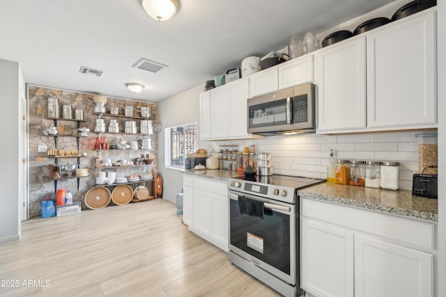 kitchen featuring light wood finished floors, visible vents, stainless steel appliances, and backsplash