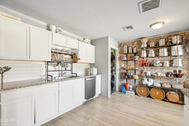 kitchen featuring dishwasher, stacked washer and dryer, a sink, and visible vents