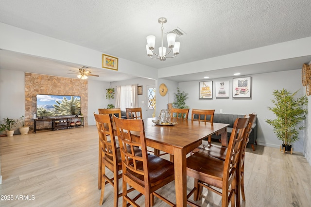 dining area with a textured ceiling, light wood finished floors, ceiling fan with notable chandelier, and visible vents