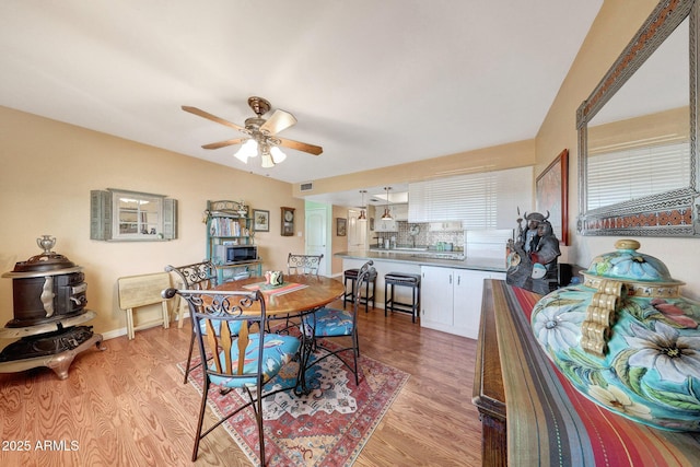 dining room with light wood finished floors, ceiling fan, and baseboards