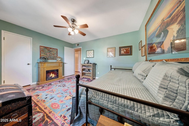 bedroom featuring a glass covered fireplace, ceiling fan, and baseboards