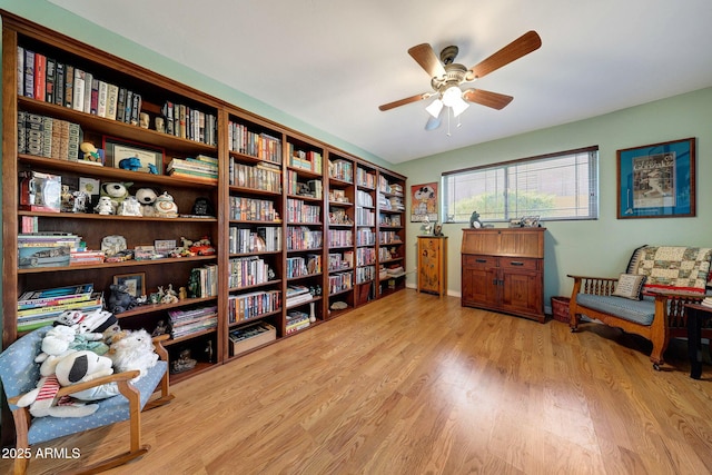 living area with light wood-style floors, a ceiling fan, and bookshelves