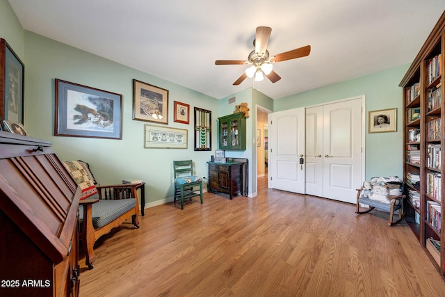living area featuring light wood finished floors, a ceiling fan, and baseboards