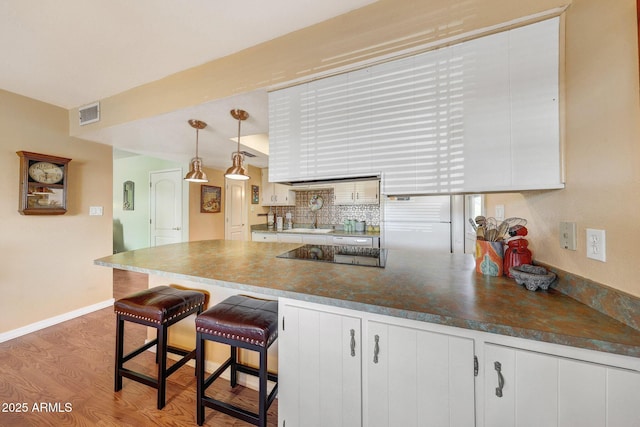 kitchen with a sink, black electric stovetop, a peninsula, baseboards, and dark countertops