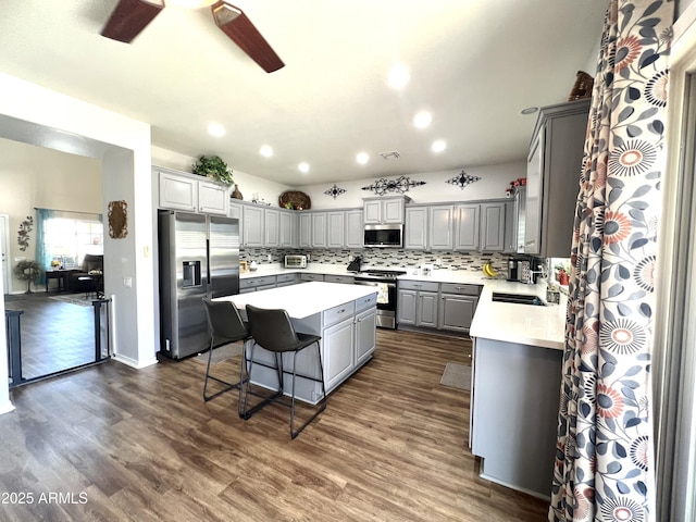kitchen featuring decorative backsplash, a kitchen island, appliances with stainless steel finishes, gray cabinetry, and dark wood-style floors
