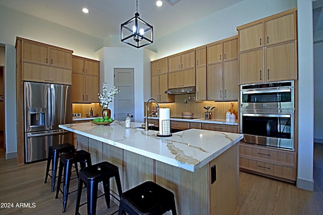 kitchen featuring a kitchen island with sink, a breakfast bar area, hardwood / wood-style floors, pendant lighting, and appliances with stainless steel finishes