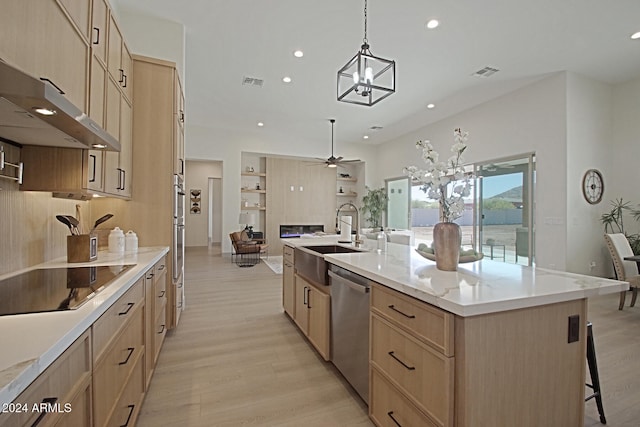 kitchen featuring dishwasher, a kitchen island with sink, sink, decorative light fixtures, and light hardwood / wood-style floors