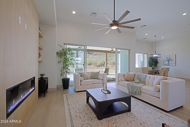 living room featuring a large fireplace, a high ceiling, light wood-type flooring, and ceiling fan