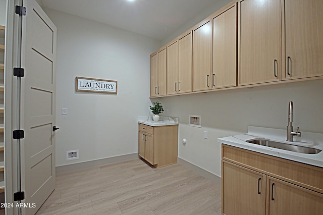 clothes washing area featuring sink, washer hookup, light hardwood / wood-style floors, and cabinets