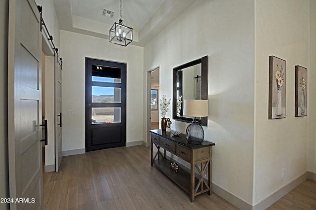 foyer entrance with a barn door, a chandelier, wood-type flooring, and a raised ceiling