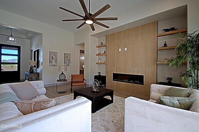 living room featuring built in features, wood-type flooring, a large fireplace, and ceiling fan