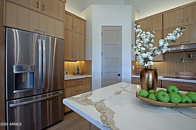 kitchen with stainless steel fridge, dark hardwood / wood-style flooring, extractor fan, light stone countertops, and cooktop