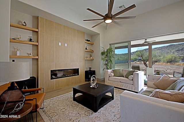 living room featuring wood-type flooring, a fireplace, built in features, ceiling fan, and a mountain view