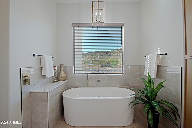 bathroom featuring tile walls, wood-type flooring, a notable chandelier, and a washtub