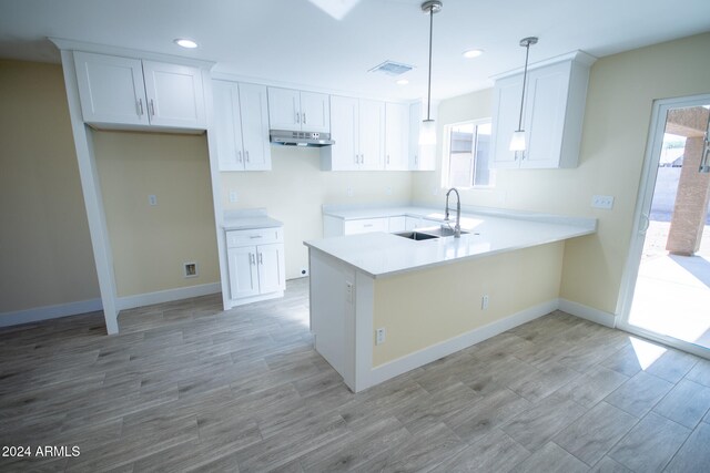 kitchen featuring kitchen peninsula, hanging light fixtures, sink, white cabinetry, and light wood-type flooring