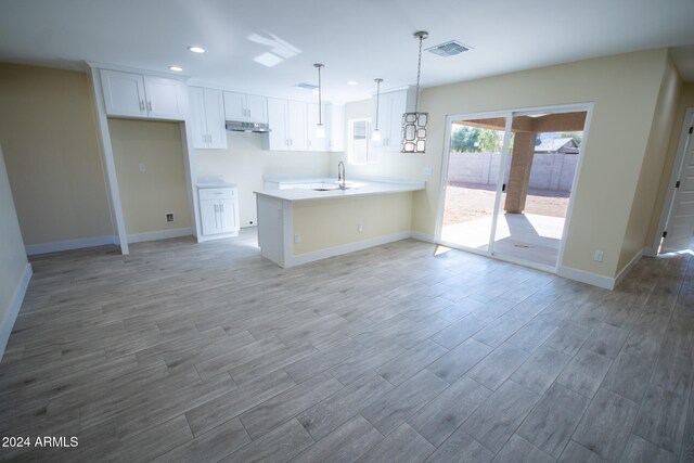 kitchen featuring light wood-type flooring, hanging light fixtures, sink, white cabinets, and kitchen peninsula