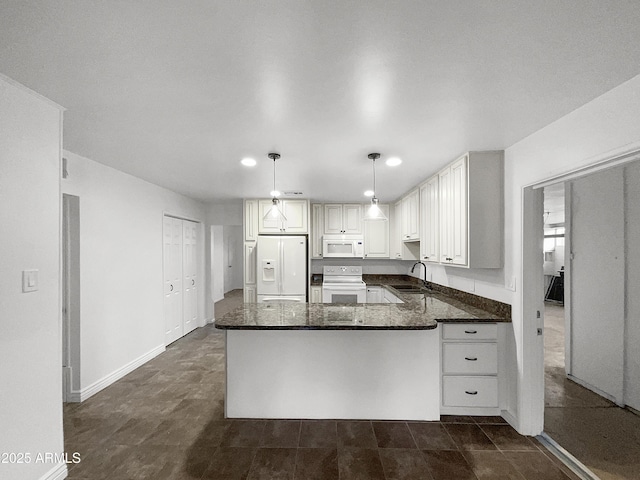 kitchen featuring a sink, white appliances, a peninsula, and dark stone countertops