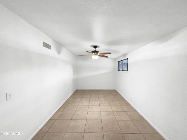 empty room featuring light tile patterned floors, visible vents, baseboards, and ceiling fan