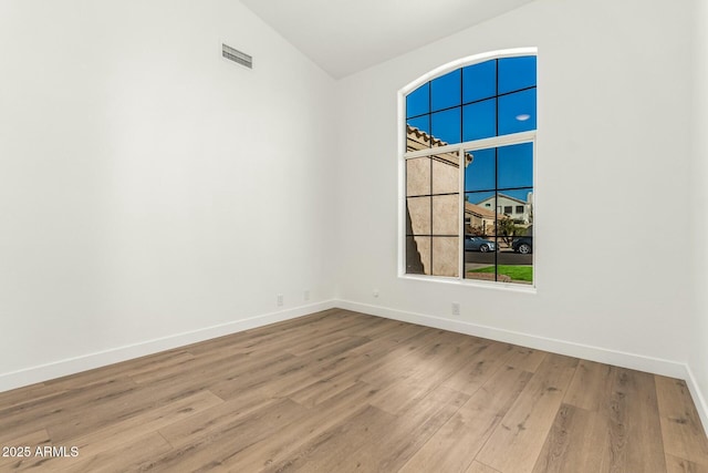 unfurnished room with lofted ceiling, wood finished floors, visible vents, and baseboards