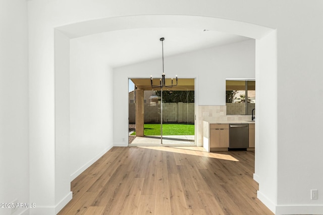 unfurnished dining area featuring lofted ceiling, baseboards, a sink, and light wood finished floors