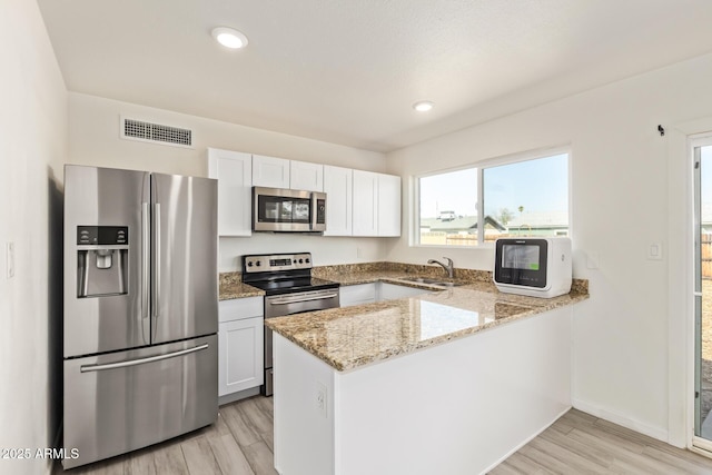 kitchen featuring stainless steel appliances, a peninsula, a sink, visible vents, and light stone countertops