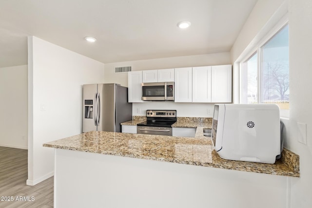 kitchen with a peninsula, light stone countertops, appliances with stainless steel finishes, and light wood finished floors