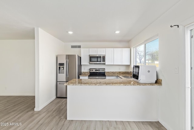 kitchen with visible vents, appliances with stainless steel finishes, white cabinets, light stone countertops, and a peninsula