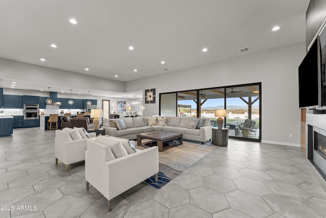 living area featuring recessed lighting, a high ceiling, visible vents, baseboards, and a glass covered fireplace