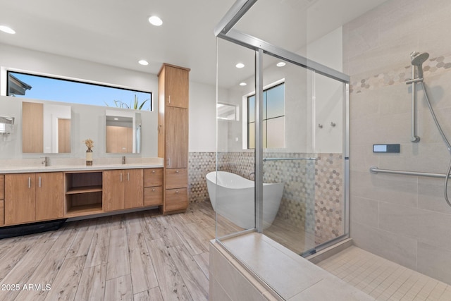 full bathroom with double vanity, tile walls, a freestanding tub, a shower stall, and a sink