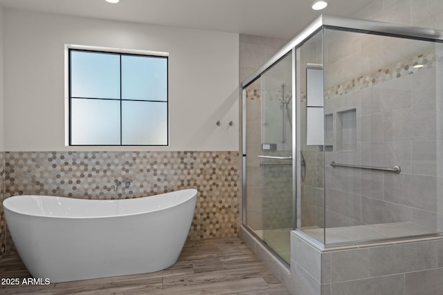 bathroom featuring a wainscoted wall, a stall shower, wood finished floors, and tile walls