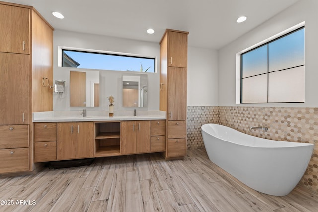 full bathroom featuring double vanity, a freestanding bath, wainscoting, a sink, and wood finished floors