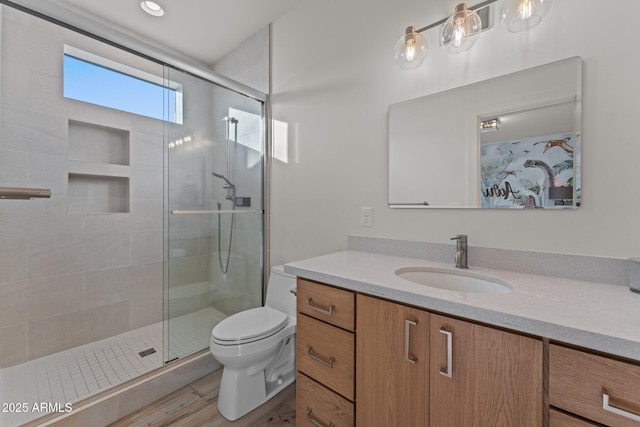 bathroom featuring wood finished floors, a shower stall, toilet, and vanity