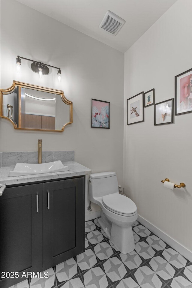 half bathroom featuring baseboards, visible vents, toilet, tile patterned floors, and vanity