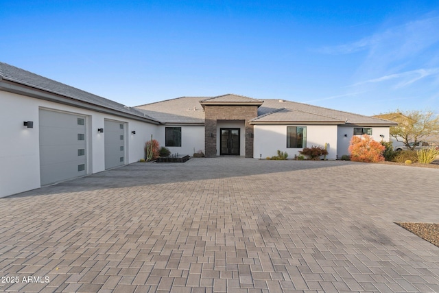 view of front facade featuring driveway, stone siding, a garage, and stucco siding