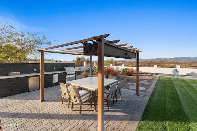 view of patio with grilling area, fence, outdoor dining area, exterior kitchen, and a mountain view