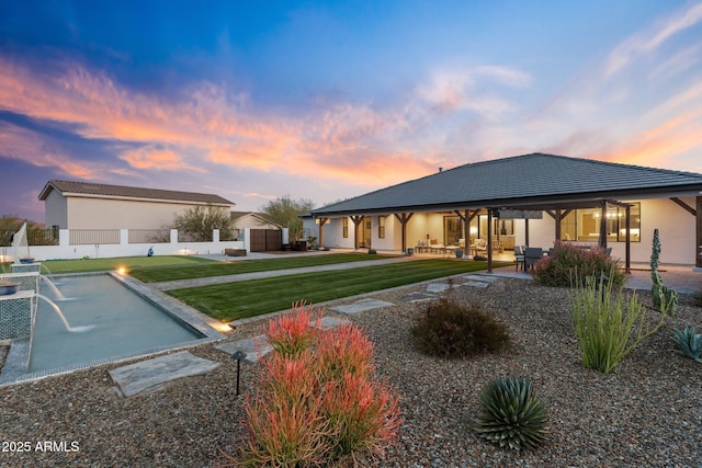 rear view of house featuring a yard, a patio area, fence, and stucco siding