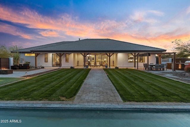 back of property at dusk featuring stucco siding, a lawn, a tiled roof, and a patio