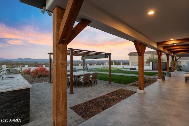 view of patio / terrace featuring outdoor dining space, a mountain view, a sink, fence, and exterior kitchen