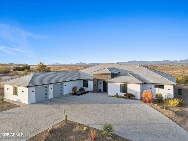 view of front of property featuring decorative driveway, a mountain view, an attached garage, and stucco siding