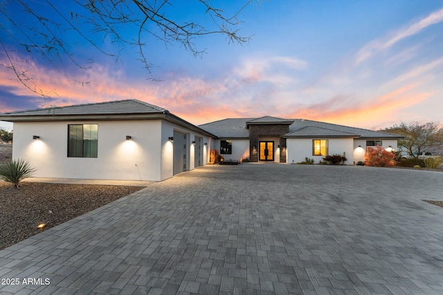 view of front of house with stone siding, decorative driveway, an attached garage, and stucco siding