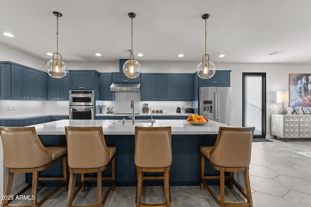 kitchen with extractor fan, blue cabinets, stainless steel appliances, light countertops, and a center island with sink