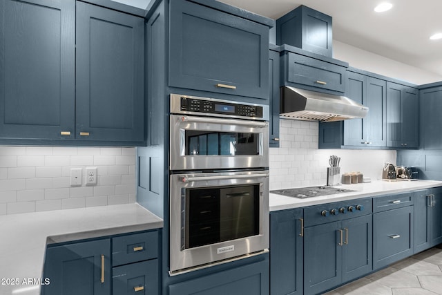 kitchen featuring tasteful backsplash, double oven, light countertops, under cabinet range hood, and gas stovetop