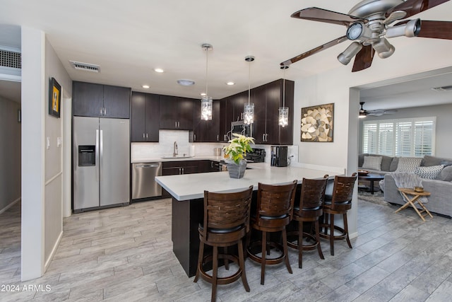 kitchen with kitchen peninsula, light wood-type flooring, a breakfast bar, stainless steel appliances, and hanging light fixtures