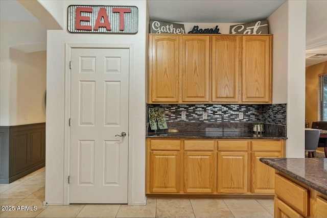 kitchen with backsplash, light tile patterned floors, and dark stone countertops